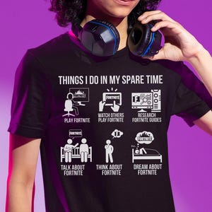 May include: Black t-shirt with the text "THINGS I DO IN MY SPARE TIME" and illustrations of activities related to the video game Fortnite. The activities include playing, watching, researching, talking, thinking, and dreaming about Fortnite.