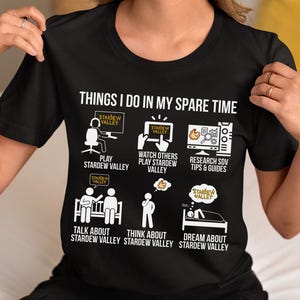 May include: Black t-shirt with the text "THINGS I DO IN MY SPARE TIME" and illustrations related to the video game Stardew Valley. The shirt features icons of playing, watching, researching, talking, thinking, and dreaming about the game.