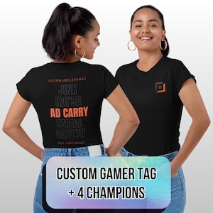 May include: Two women wearing black t-shirts with custom gamer tag and champion names. The back of one shirt displays "USERNAME123#NA1" and champion names in black and orange. The front of the other shirt has a small logo.