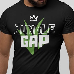 May include: Black t-shirt featuring the text "JUNGLE GAP" in white with a black outline, a white crown, and green leaf shapes. The t-shirt has a crew neck design.