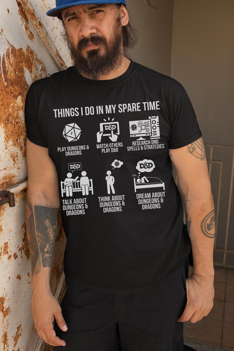 May include: Black t-shirt with white text and graphics. The shirt reads "THINGS I DO IN MY SPARE TIME" above six illustrations related to Dungeons & Dragons. The illustrations include a die, a D&D logo, and a person in bed.