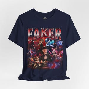 Op de afbeelding: Een marineblauw t-shirt met een grafische print van een League of Legends-speler, Faker, omringd door personages uit het spel. De tekst "FAKER" is in rode en witte letters boven de print gedrukt.