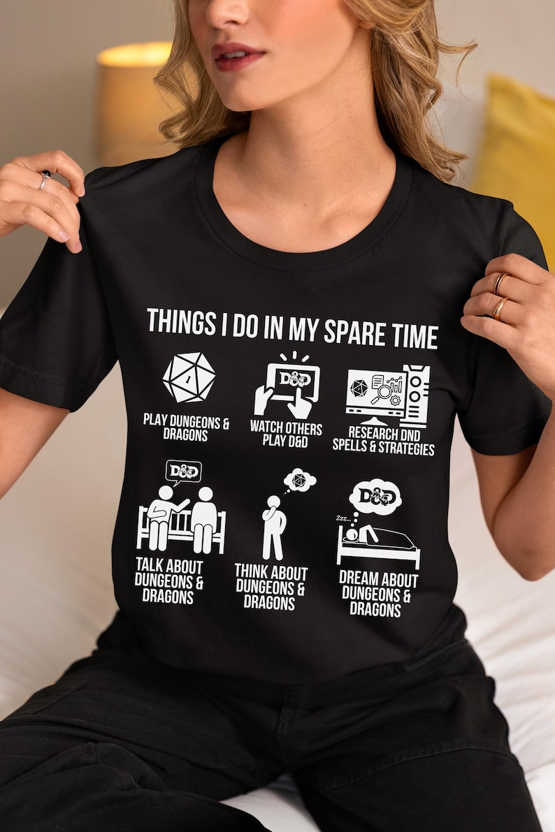 May include: Black t-shirt with white text and graphics. The shirt reads "THINGS I DO IN MY SPARE TIME" above illustrations of dice, a computer screen, and people. The theme is Dungeons & Dragons.