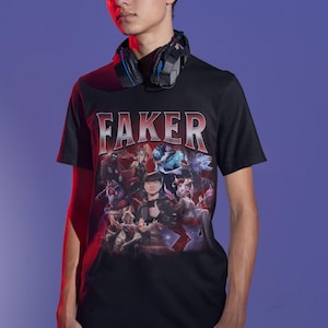 Op de afbeelding: Zwart T-shirt met een grafische print van een videogamepersonage, "Faker", en andere personages. Het shirt heeft een rood-wit verloopontwerp.