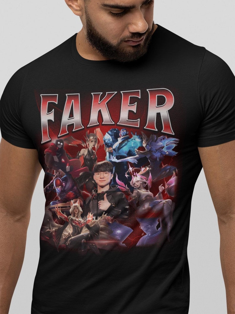 Op de afbeelding: Zwart T-shirt met een grafische print van een League of Legends-speler, Faker, omringd door verschillende personages uit het spel. De tekst "FAKER" is in grote witte letters bovenaan het ontwerp gedrukt.