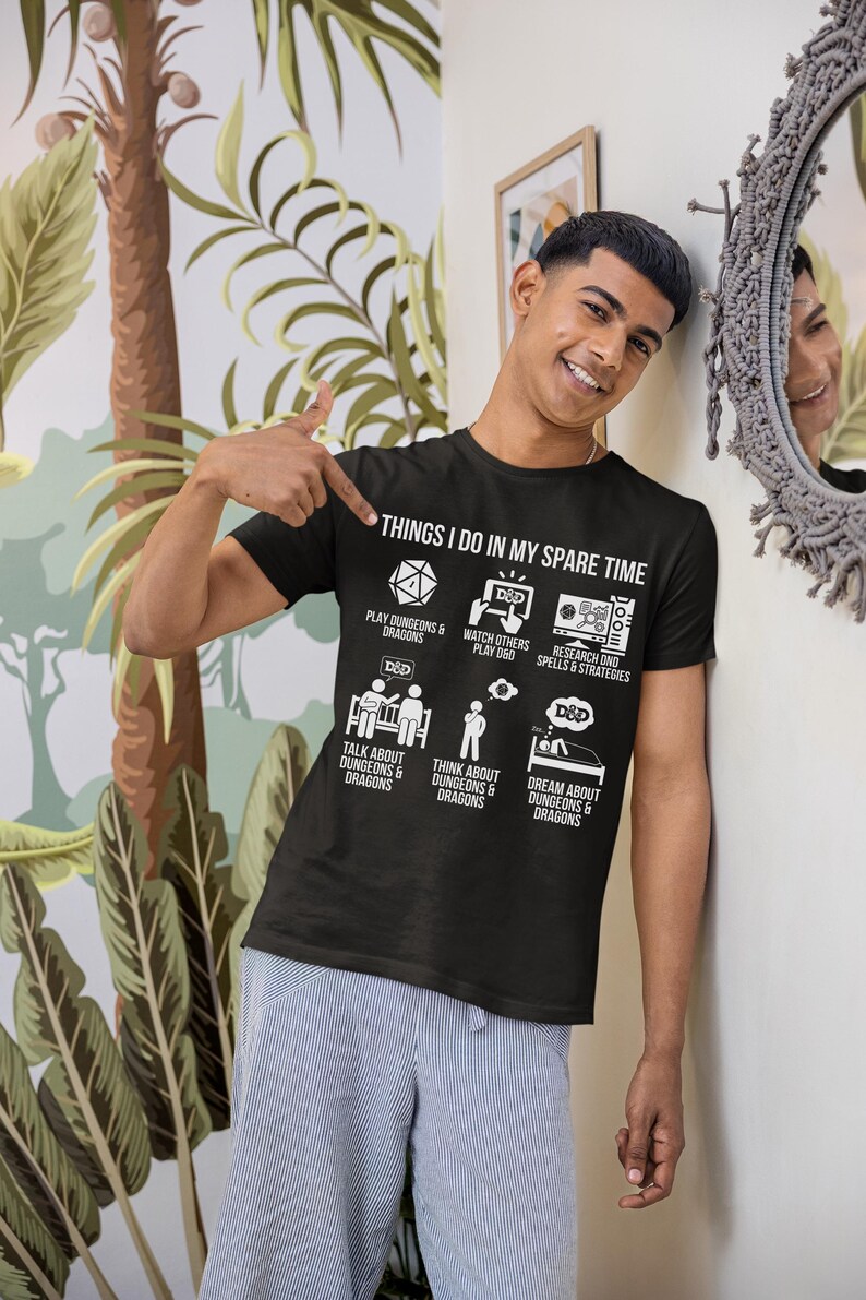May include: Black t-shirt with the text "THINGS I DO IN MY SPARE TIME" and illustrations of activities related to Dungeons & Dragons. The shirt features icons and text describing various D&D-related pastimes.