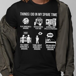May include: Black t-shirt with white graphic text and illustrations about Dungeons & Dragons. The text reads "THINGS I DO IN MY SPARE TIME" with icons for playing, watching, researching, talking, thinking, and dreaming about D&D.