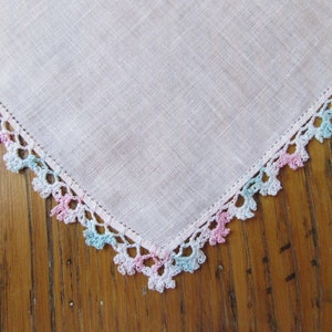 Puede incluir: Un pañuelo de lino blanco con un delicado borde de ganchillo en rosa, azul y blanco.