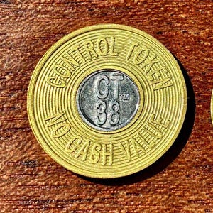 May include: A gold-colored token with the words "CONTROL TOKEN" and "NO CASH VALUE" around the edge. The center has a silver circle with "CT 38" in the middle. The token is on a wooden surface.