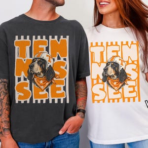 May include: A charcoal grey t-shirt and a white t-shirt, each featuring a graphic of a dog wearing a helmet and bandana, with the orange text "TEN SEE" layered over vertical stripes. The shirts are labelled "Pepper" and "White" respectively.