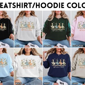 May include: A selection of sweatshirts and hoodies in various colors, including black, ash, forest green, light pink, light blue, white, navy, and sand. Each sweatshirt features a graphic of geese and the text "off to fix a latch."