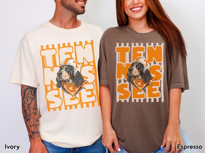 May include: An ivory t-shirt and an espresso t-shirt, each featuring a graphic of a hound dog wearing a football helmet and a bandana. The text "TEN SEE" is printed in large orange letters behind the dog, set against a background of vertical stripes.