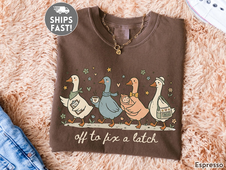 May include: Espresso-colored t-shirt featuring a whimsical illustration of five geese walking in a row. Each goose is uniquely accessorized, carrying items like a clipboard, coffee, a baby, and a bag. The text "off to fix a latch" is printed below the geese.