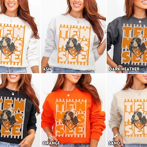 May include: A collection of six crewneck sweatshirts in white, ash, dark heather, black, orange, and sand. Each features a graphic of a dog wearing a football helmet and bandana, with the text TEN SEE overlaid on vertical orange stripes.