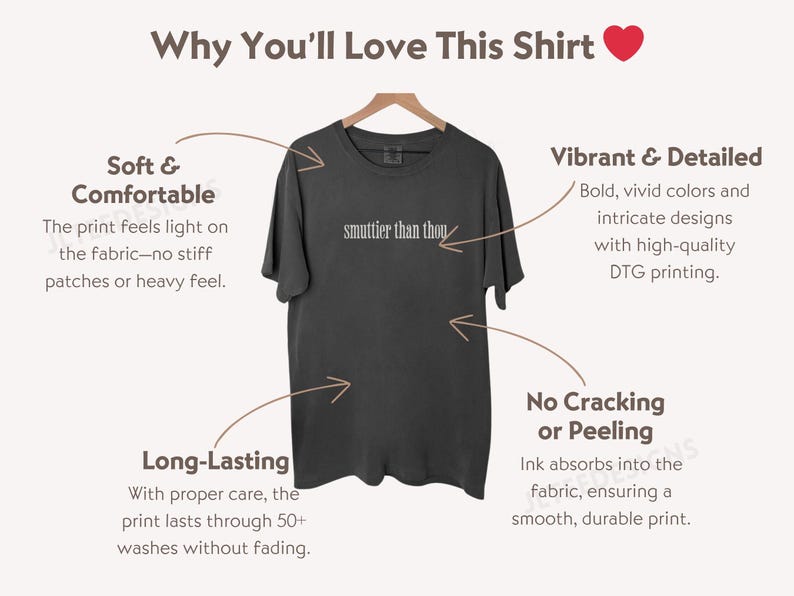 Puede incluir: Camiseta gris oscuro con el texto "smuttier than thou" en blanco. La camiseta se muestra en una percha de madera. La imagen destaca la tela suave y c&oacute;moda de la camiseta y su impresi&oacute;n duradera.