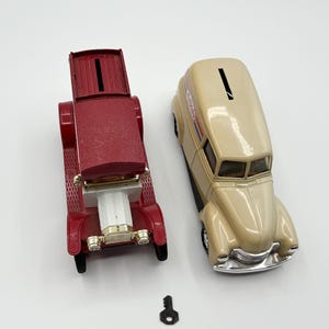 May include: Two vintage car-shaped metal banks, one red and one beige, with coin slots on top. A small black key is also present. The red car has a convertible top. The beige car has the text "Candy Avenue" on the side.