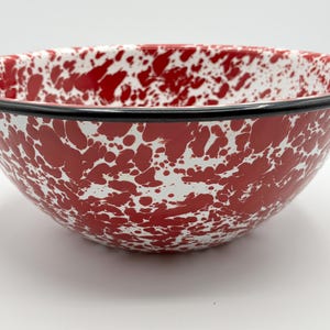 May include: A red and white enamel mixing bowl with a black rim. The bowl has a speckled pattern of red and white. This kitchenware item is ideal for mixing ingredients or serving food.