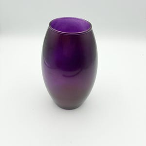 May include: A deep purple glass vase with an oval shape. The vase has a gradient effect, transitioning from a lighter purple at the top to a darker shade at the base. The interior is a vibrant purple.
