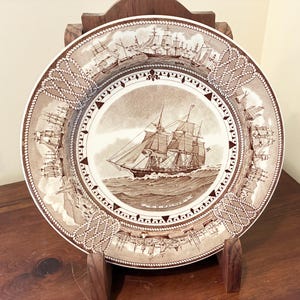 May include: A white ceramic mug with a black handle and the text "But First, Coffee" in a bold, black font. The mug is set against a blurred background, suggesting a cozy setting. The mug appears to be approximately 4 inches tall.