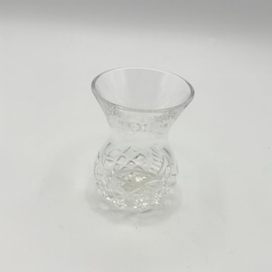 May include: A clear, small glass vase with a flared top and a textured, diamond-patterned lower half. The vase is empty and sits on a white surface. The design is simple and elegant.