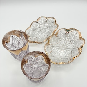 May include: Four-piece crystal glassware set. Two small, clear, patterned bowls with gold rims and two matching glasses with gold rims. The glassware is arranged on a white surface.