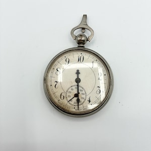May include: A silver pocket watch with a white face and black numerals. The watch has a small seconds dial and a loop at the top for a chain. The watch face reads "PATENT APP".