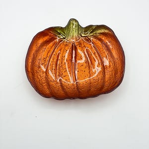May include: A pumpkin-shaped glass dish featuring a textured, translucent orange surface with a green stem detail at the top. The bowl has a ribbed design that mimics the natural ridges of a pumpkin, with a glossy finish and a clear glass edge.
