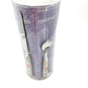 May include: A Pfaltzgraff flatware set in a clear cylindrical plastic container. The set includes a silver knife and spoon with white handles featuring a colorful floral pattern. The packaging displays the Pfaltzgraff brand name in white text.