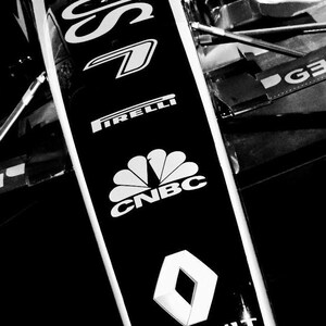 May include: Black and white photo of a race car with the word "Lotus" and the logos "Pirelli", "CNBC", "Renault" on the side.