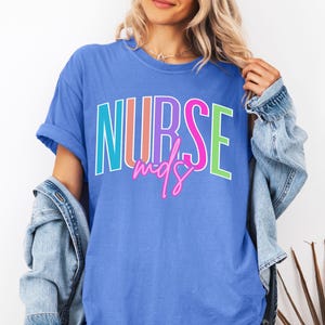 May include: A blue t-shirt with the words "NURSE mds" in colorful block letters. The shirt has short sleeves and a relaxed fit. A denim jacket is draped over the shoulders.