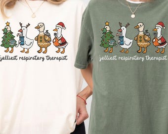 May include: Ivory and moss green t-shirts with a whimsical design. The shirts feature a cartoon illustration of four geese dressed in Christmas attire, holding medical equipment, with the text "jalliest respiratory therapist".