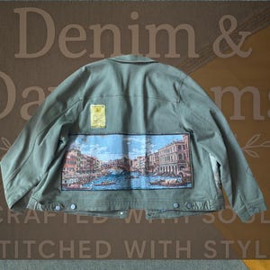 May include: An olive green denim jacket with a colorful tapestry back panel depicting a canal scene. The jacket has a button-down front, a small label, and the words "Denim & Dams" and "Crafted with Soul Stitched with Style" are visible.