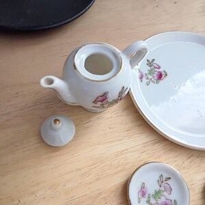 Pu&ograve; includere: Un servizio da t&egrave; in miniatura in porcellana bianca con finiture dorate e decorazioni floreali. Il set include una piccola teiera, un coperchio, un piattino e un piatto. La teiera &egrave; rotonda con manico e beccuccio.