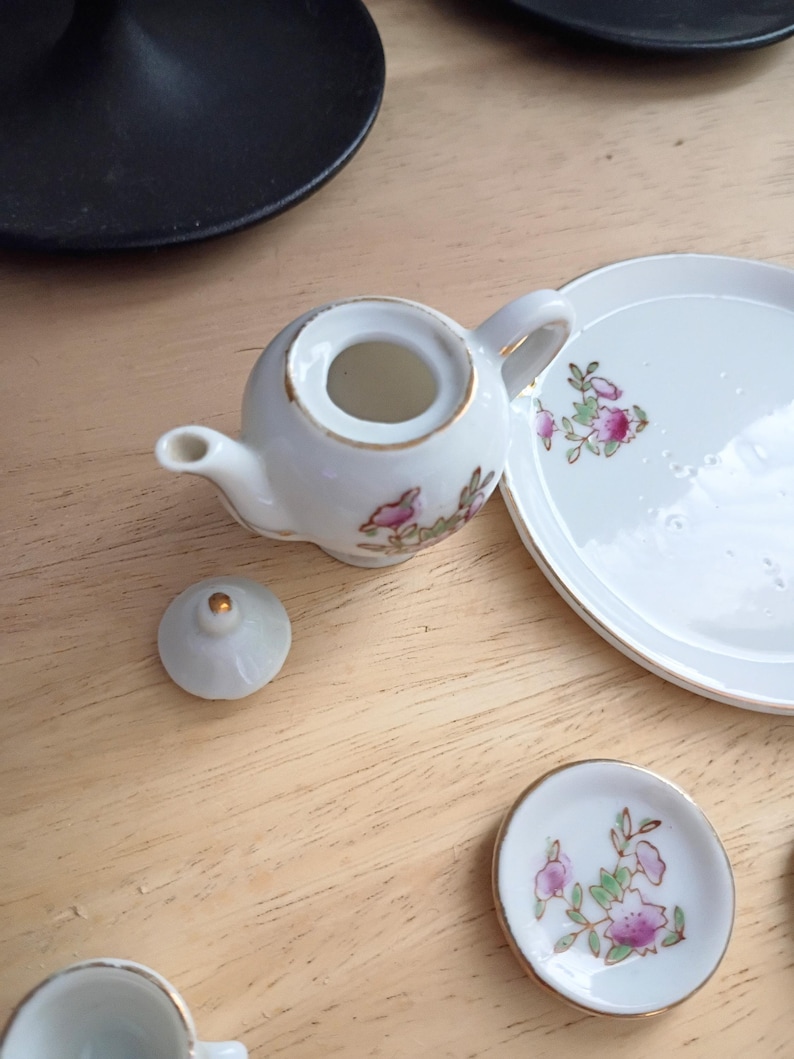 Pu&ograve; includere: Un servizio da t&egrave; in miniatura in porcellana bianca con finiture dorate e decorazioni floreali. Il set include una piccola teiera, un coperchio, un piattino e un piatto. La teiera &egrave; rotonda con manico e beccuccio.