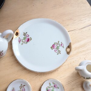 Pu&ograve; includere: Un servizio da t&egrave; in porcellana bianca con finiture dorate e decorazioni floreali. Il set include un vassoio, piattini e una lattiera. Il motivo floreale presenta fiori rosa e foglie verdi.