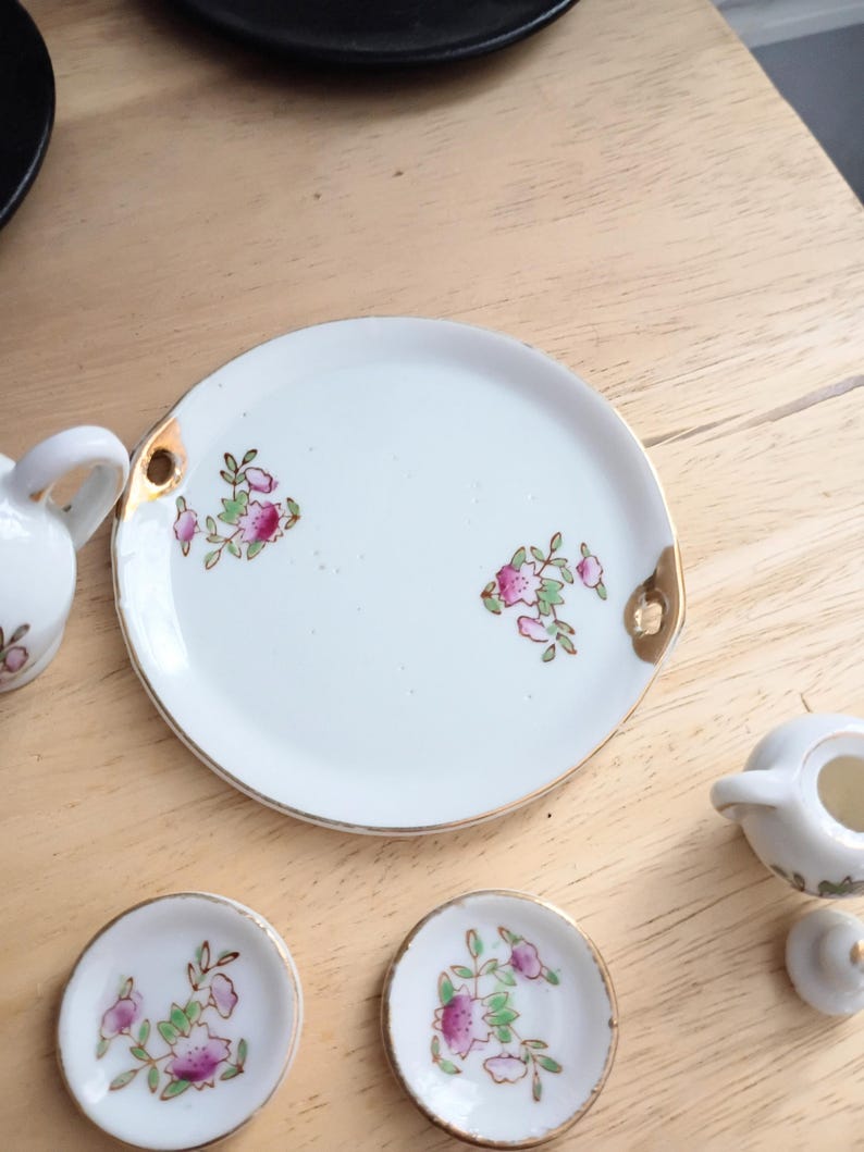 Pu&ograve; includere: Un servizio da t&egrave; in porcellana bianca con finiture dorate e decorazioni floreali. Il set include un vassoio, piattini e una lattiera. Il motivo floreale presenta fiori rosa e foglie verdi.