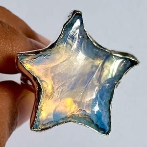 Peut inclure: Bague en forme d'étoile avec un anneau argenté. L'étoile présente un aspect irisé avec des nuances de bleu, de jaune et de blanc. Ce bijou est une pièce unique.