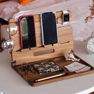 Può includere: Un supporto in legno per telefono e orologio con slot per due telefoni, un orologio e un paio di occhiali. C'è anche spazio per un portafoglio e una penna. Il supporto è in legno scuro e ha una finitura naturale.
