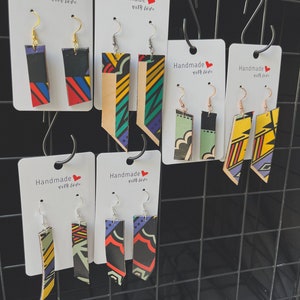 May include: Assortment of colorful handmade earrings with geometric patterns. The earrings are displayed on white cards with the text "Handmade with love".