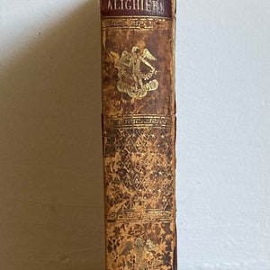 May include: A vintage book with a worn leather cover. The title on the spine reads "LA DIVINA COMEDIA DI DANTE ALIGHIERI".