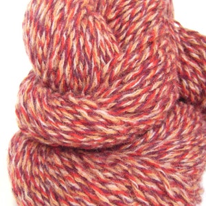 May include: A skein of yarn in a multi-colored blend of red, orange, white, and purple. The yarn is soft and fluffy, and it is perfect for knitting or crocheting.