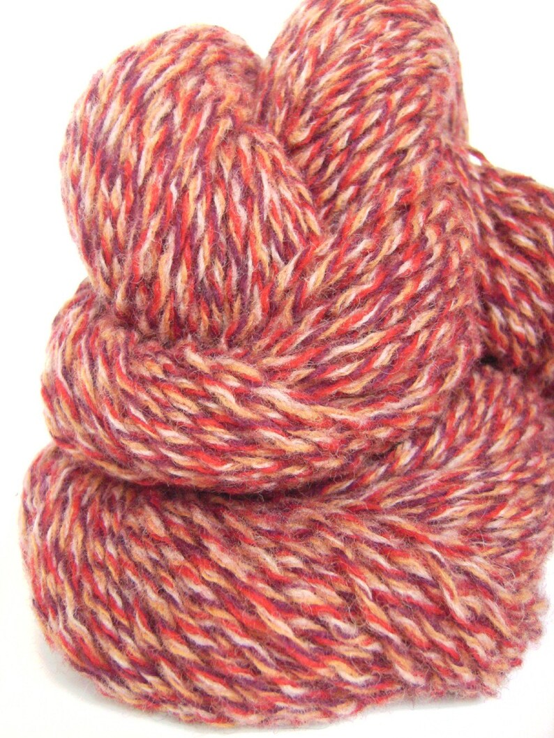 May include: A skein of yarn in a multi-colored blend of red, orange, white, and purple. The yarn is soft and fluffy, and it is perfect for knitting or crocheting.