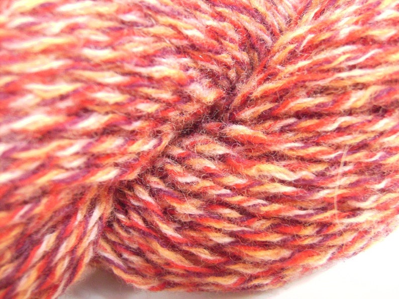 May include: A close-up of a ball of yarn with a mix of red, orange, white, and purple colors.