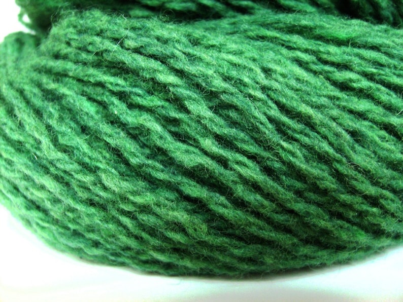 May include: A close-up of a skein of deep green yarn. The yarn is soft and fluffy, and it has a slightly textured surface.