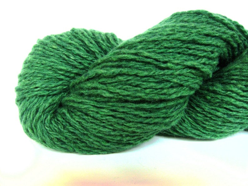 May include: A skein of dark green yarn, made of wool, is shown in a close-up view. The yarn is soft and fluffy, and it is perfect for knitting or crocheting.