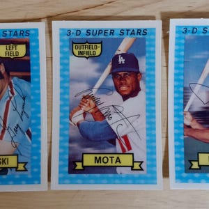 May include: Three baseball cards featuring baseball players with their names and positions printed on the cards. The cards are blue and yellow with a white border. The players are holding baseball bats and wearing baseball uniforms. The cards are from the 3-D Super Stars series.