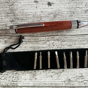 May include: A wooden pen with a silver clip and tip, and a black velvet pouch containing several silver screwdriver bits. The pen has a reddish-brown finish. The bits are of various shapes and sizes.
