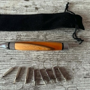 May include: A wooden pen with a light brown and orange wood grain pattern, silver accents, and a black velvet carrying case. Several silver pen tips are also included.