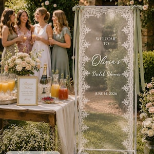 K&ouml;nnte beinhalten: Ein hohes, rechteckiges, transparentes Acryl-Willkommensschild mit wei&szlig;er Spitzenbord&uuml;re und salbeigr&uuml;nen Schleifen an den oberen Ecken. Das Schild tr&auml;gt den Text: WELCOME TO Olivia's Bridal Shower JUNE 14, 2026. Es misst 75x200 cm.