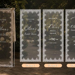 K&ouml;nnte beinhalten: Vier hohe, rechteckige, transparente Acryl-Willkommensschilder f&uuml;r eine Brautparty, jedes mit einem wei&szlig;en Spitzenmuster-Rand. Der Text lautet Welcome to Olivia's Bridal Shower, June 14, 2026, mit Variationen im Layout und dekorativen Schleifensymbolen.